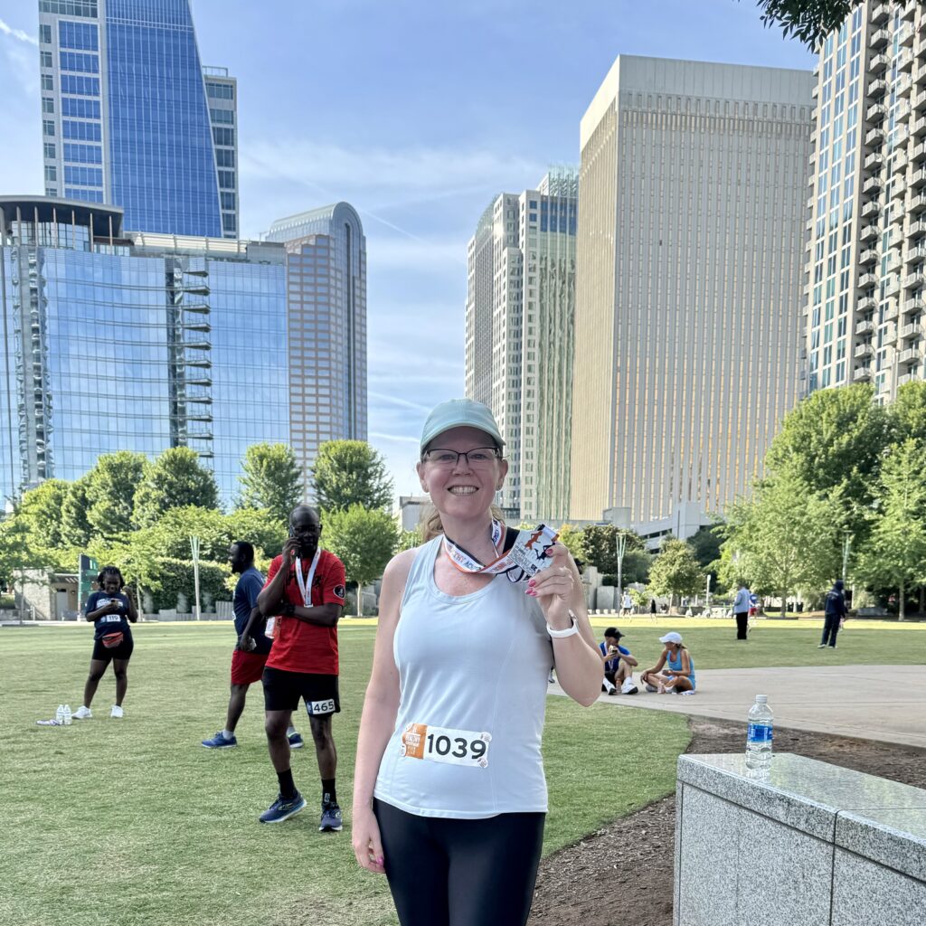 Kristin standing at the finish line holding her medal with the Charlotte skyline in the background.